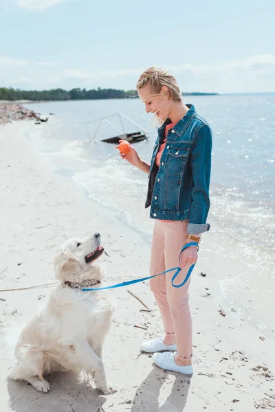 Жінка грає в м'яч із золотою собакою-ретривером на морському березі — стокове фото