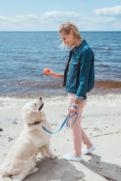 Belle femme jouant au ballon avec un chien amical sur le bord de mer — Photo de stock
