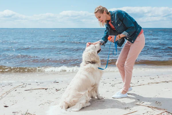 Happy woman playing ball with golden retriever on sea shore — Stock Photo