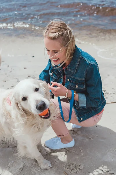 Mulher loira brincando com cão golden retriever na costa arenosa — Fotografia de Stock