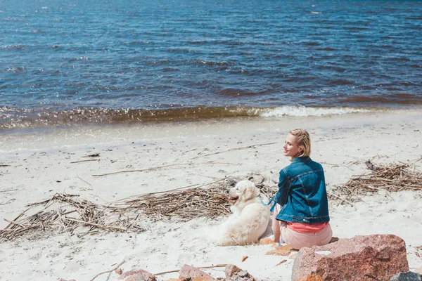 Vista posteriore della donna seduta sulla riva con cane golden retriever vicino al mare — Foto stock