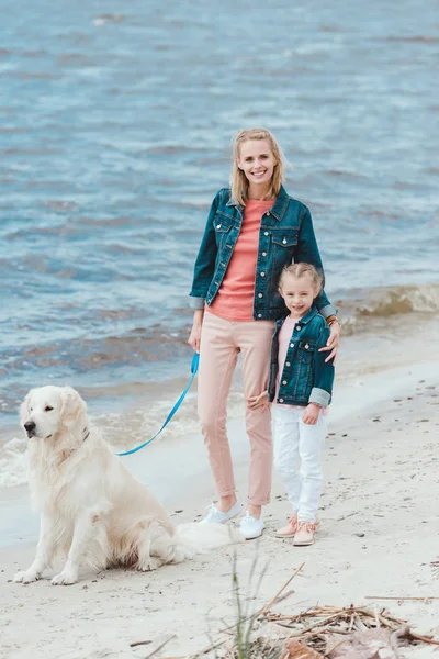 Hermosa familia caminando con perro golden retriever cerca del mar - foto de stock