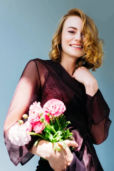 Vista de ángulo bajo de hermosa chica sosteniendo flores y sonriendo a la cámara aislada en gris - foto de stock