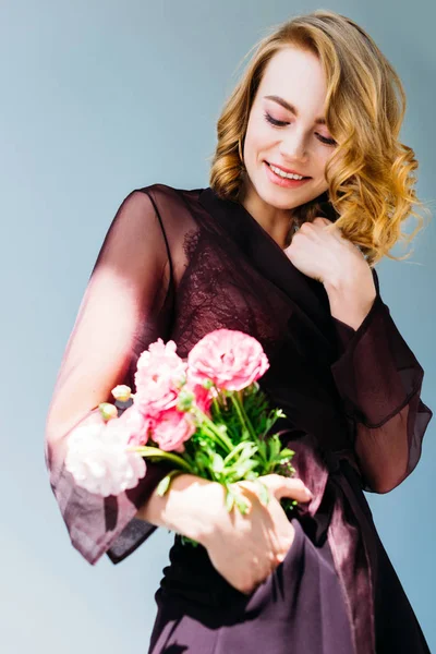 Vista basso angolo di bella ragazza sorridente che tiene fiori rosa isolati su grigio — Foto stock