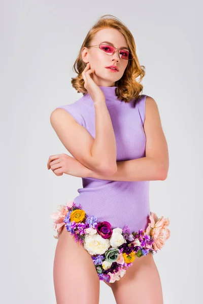 Hermosa mujer joven en gafas de sol y bragas hechas de flores mirando a la cámara aislada en gris - foto de stock