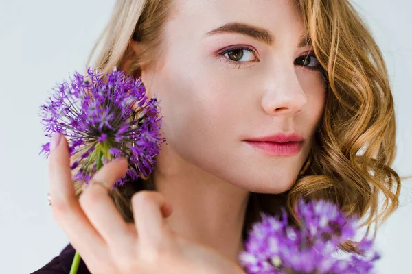 Schönes Mädchen mit frischen violetten Blumen und Blick in die Kamera isoliert auf grau — Stockfoto