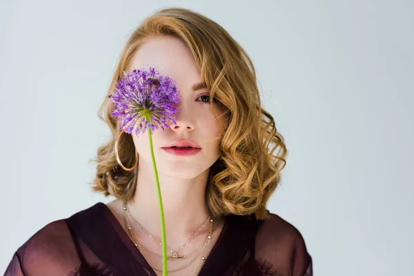 Schöne junge Frau mit zarter frischer Blume und Blick in die Kamera isoliert auf grau — Stockfoto