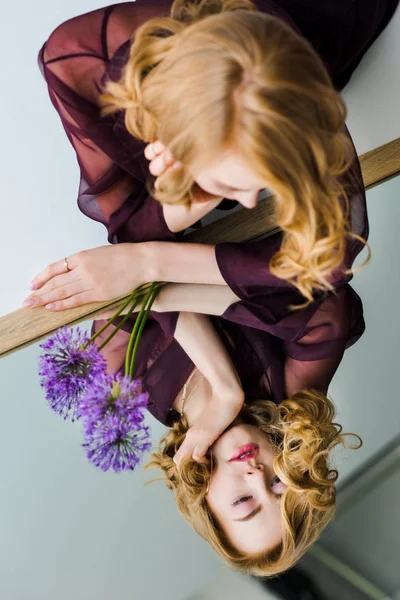 Молодая женщина, глядя на отражение, лежа на зеркале с фиолетовыми цветами — стоковое фото