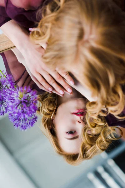 Selective focus of young woman looking at reflection while lying on mirror with blue flowers — Stock Photo