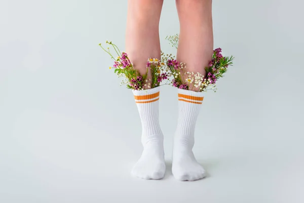 Plan recadré de fille en chaussettes avec des fleurs fraîches isolées sur gris — Photo de stock