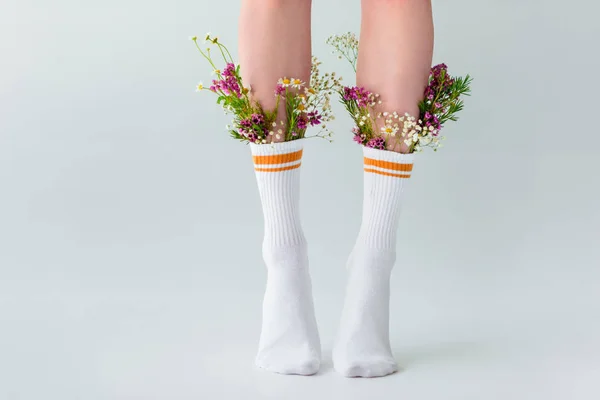 Частичный вид женских ног в носках со свежими цветами, изолированными на сером — стоковое фото