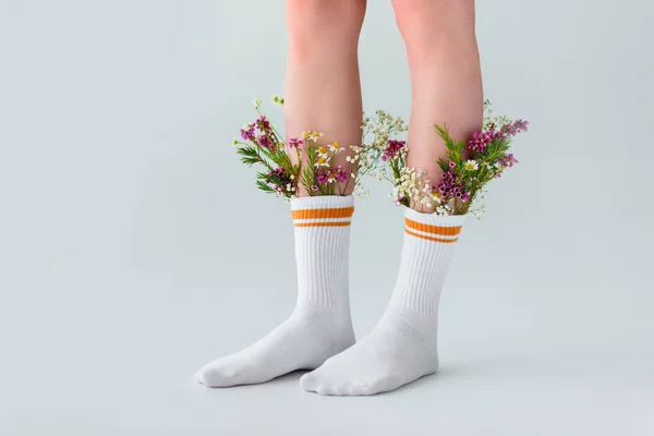 Plan recadré de jambes féminines en chaussettes avec des fleurs fraîches isolées sur gris — Photo de stock