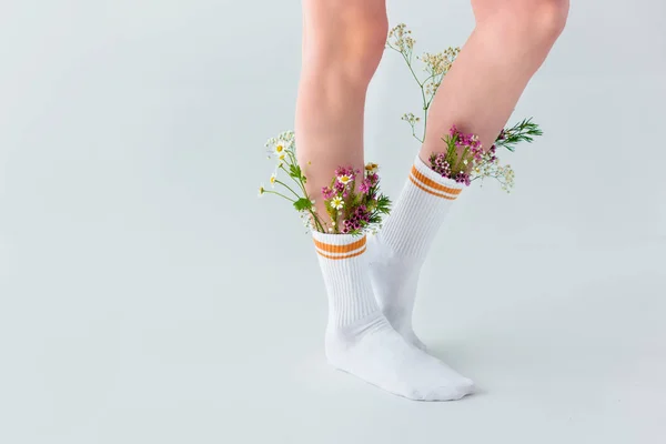 Vista parcial de mujer joven en calcetines con hermosas flores frescas aisladas en gris - foto de stock
