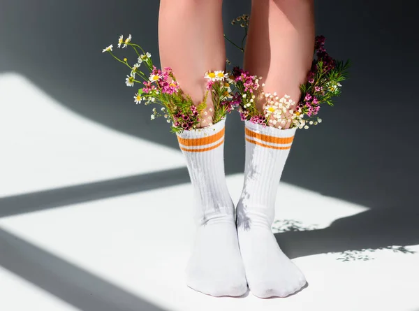 Cropped shot of girl with beautiful flowers in socks standing on grey — Stock Photo