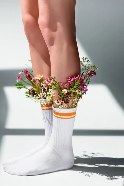 Primo piano vista parziale di giovane donna con bellissimi fiori in calzini in piedi sul grigio — Foto stock