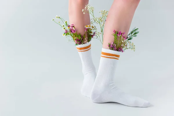 Gros plan vue partielle des pattes des femelles avec des fleurs fraîches dans des chaussettes isolées sur gris — Photo de stock