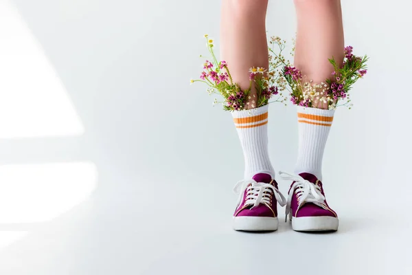 Cropped shot of girl with fresh flowers in socks on grey — Stock Photo