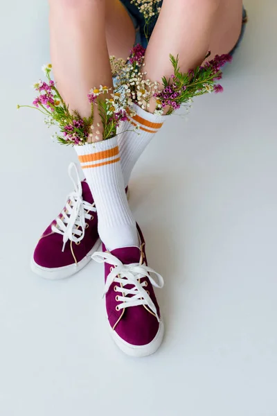 Plan recadré de jeune femme avec des fleurs en chaussettes assis isolé sur gris — Photo de stock