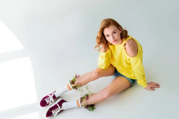 High angle view of beautiful girl looking at camera while sitting with flowers in socks on grey — Stock Photo