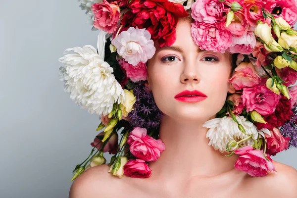 Портрет великолепной обнаженной женщины с красивыми цветами на голове, смотрящей в камеру, изолированную на сером — стоковое фото