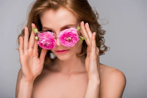 Bela jovem mulher nua ajustando óculos com flores e olhando para a câmera isolada no cinza — Fotografia de Stock