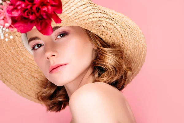 Retrato de hermosa mujer joven en sombrero con hermosas flores mirando a la cámara aislada en rosa - foto de stock