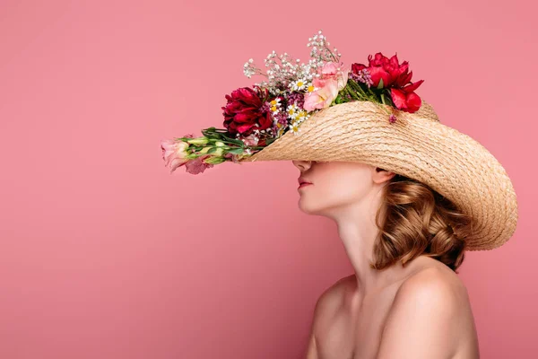Вид сбоку молодой обнаженной женщины в шляпе с цветами, изолированными на розовом фоне — стоковое фото