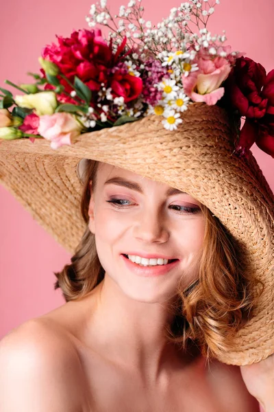 Retrato de hermosa chica desnuda sonriente con sombrero de mimbre con flores aisladas en rosa - foto de stock