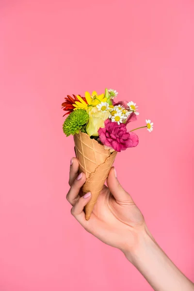 Vista parcial de cerca de la mujer sosteniendo cono de helado con hermosas flores aisladas en rosa - foto de stock