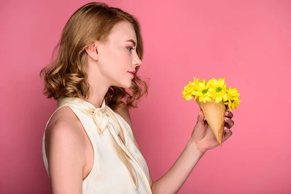 Vista lateral de hermosa chica sosteniendo cono de gofre con flores amarillas en rosa - foto de stock