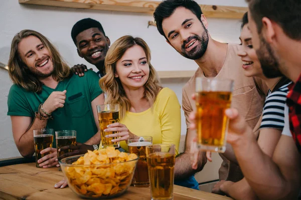 Amigos multiculturales felices con cerveza y patatas fritas viendo el partido de fútbol y hablando en el bar - foto de stock