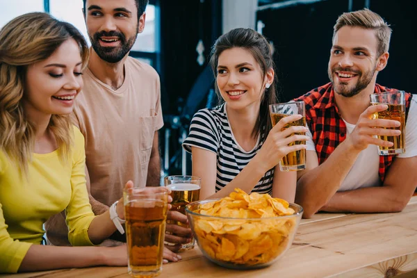 Smiling group of friends with beer and bowl of chips sitting at bar counter during watch of soccer match — Stock Photo