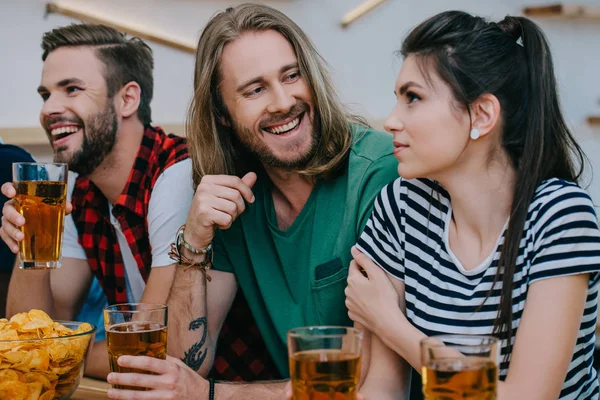 Улыбающаяся группа друзей, пьющих пиво и смотрящих футбольный матч в баре — стоковое фото