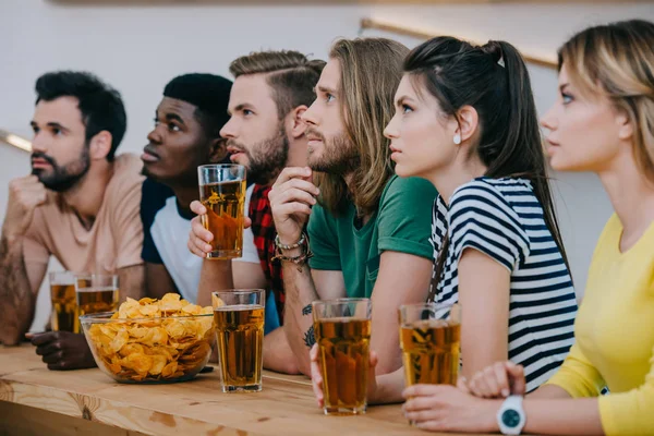 Gruppo di amici multiculturali bere birra e guardare partita di calcio al bar — Foto stock