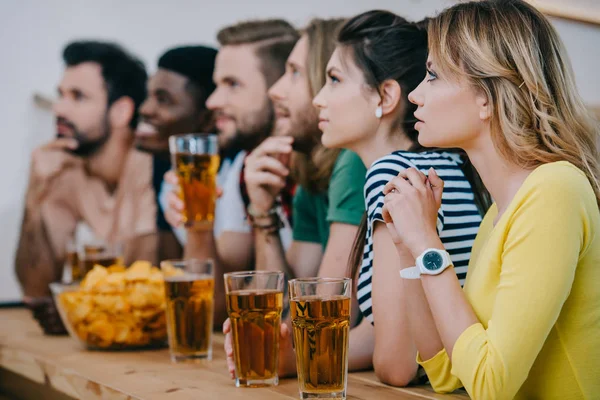 Vista lateral del grupo de amigos multiculturales bebiendo cerveza y viendo el partido de fútbol en el bar - foto de stock