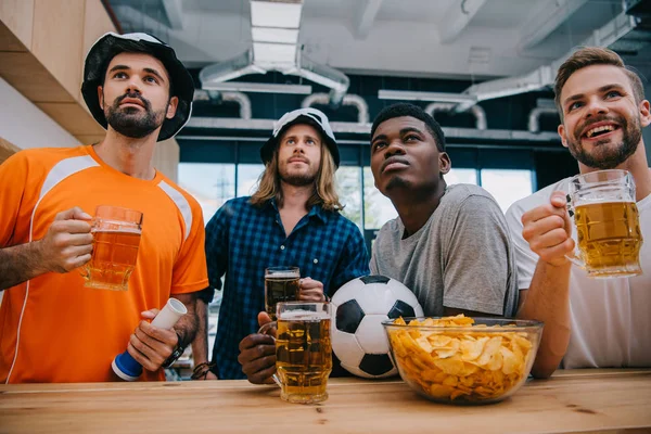 Концентрированная мультикультурная группа футбольных болельщиков с пивом, смотрящая футбольный матч в баре — стоковое фото
