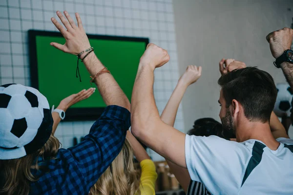 Rear view of football fans celebrating and gesturing by hands during watch of soccer match on tv screen at bar — Stock Photo