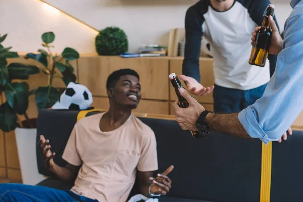 Vista parcial del hombre dando botellas de cerveza a amigos multiétnicos sonrientes en casa - foto de stock