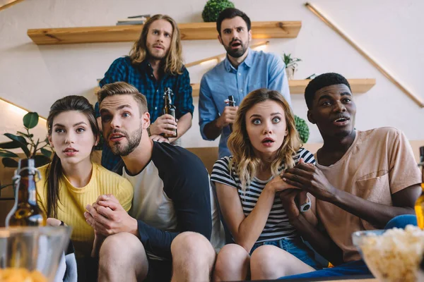 Chocado grupo de amigos multiculturais sentados no sofá e assistindo jogo de futebol em casa — Fotografia de Stock
