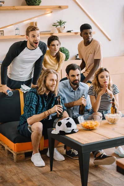Young multicultural friends with beer bottles watching football match at home — Stock Photo