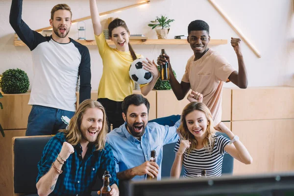 Multicultural friends with soccer ball and beer bottles doing yes gestures during watch of  football match at home — Stock Photo