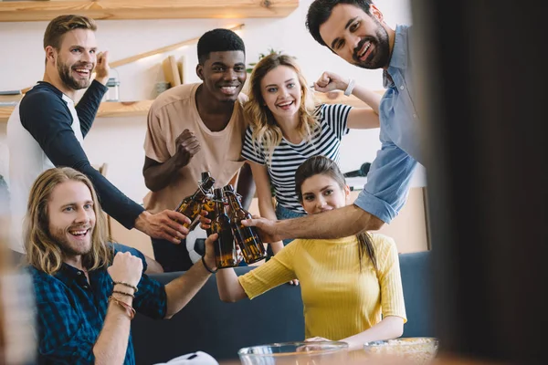 Multicultural friends celebrating and clinking beer bottles during soccer match — Stock Photo