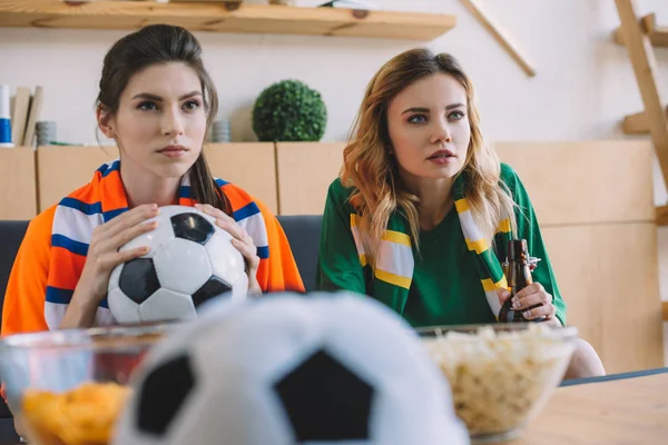 Fanáticos del fútbol femenino enfocados en diferentes camisetas y bufandas viendo el partido de fútbol en casa - foto de stock