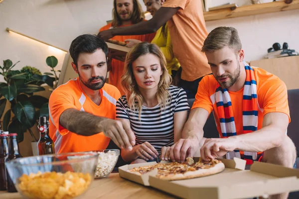 Grupo de amigos tomando rebanadas de pizza de la caja en la mesa en casa - foto de stock