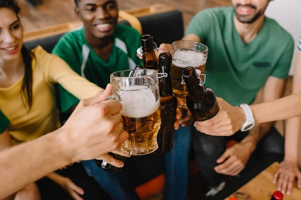 Vista de primer plano de los aficionados al fútbol multicultural celebrando y tintineo botellas de cerveza y vasos - foto de stock