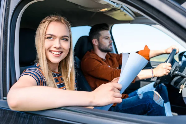 Joven mujer sonriente sentada con mapa en las manos mientras su novio conduce el coche - foto de stock