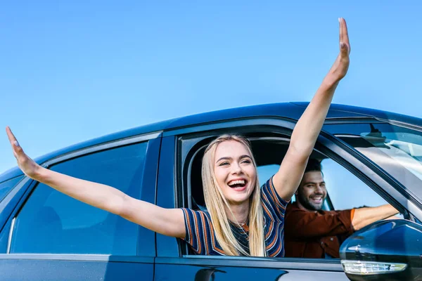 Jovem feliz com os braços largos inclinados para fora da janela do carro, enquanto seu namorado carro de condução — Fotografia de Stock