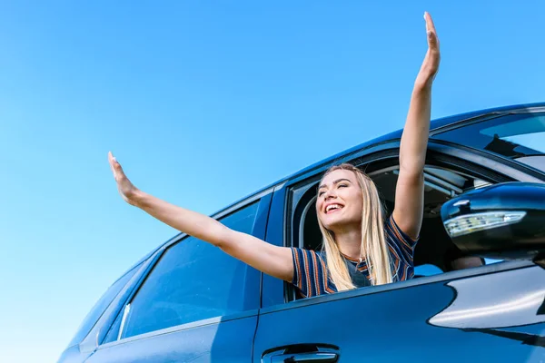 Vue à angle bas de la jeune femme avec de larges bras appuyés par la fenêtre de la voiture contre le ciel bleu — Photo de stock