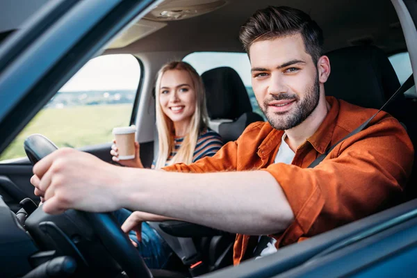Retrato de jovem sentado ao volante do carro e sua namorada com xícara de papel de café — Fotografia de Stock