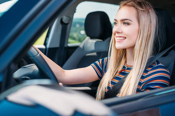 Крупным планом снимок улыбающейся молодой женщины за рулем автомобиля — стоковое фото